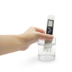 Hand holding water quality meter tester submerged in drinking glass, isolated on white background. Measuring harmful impurities, purifying water for healthy eating.