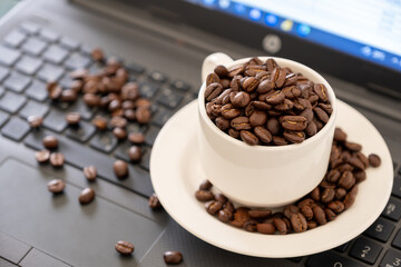 Cup of coffee that full of coffee beans on laptop background with rim light represents working...