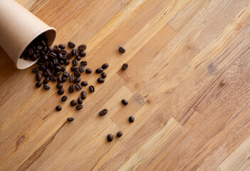 Paper cup of coffee with spilled coffee beans nature friendly on wooden background from top view...