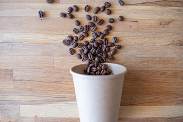 Paper cup of coffee with spilled coffee beans nature friendly on wooden background from top view with mock up space
