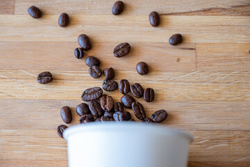 Paper cup of coffee with spilled coffee beans nature friendly on wooden background from top view with mock up space
