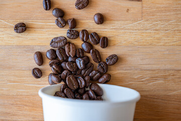 Paper cup of coffee with spilled coffee beans nature friendly on wooden background from top view with mock up space
