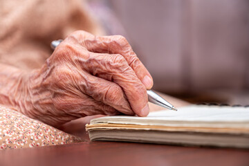 close up wrinkled hands for elderly person writing notes on his note book