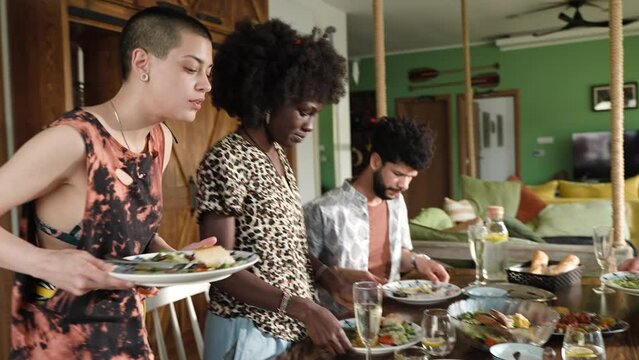 Young and diverse group of friends finishing their lunch together and cleaning up leftovers in their rented lake house on vacation