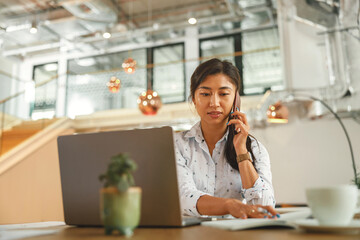 Woman office manager talking phone with client and making notes while sitting the desk in office 