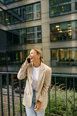 Smiling woman office worker is standing on modern building background and looking at side