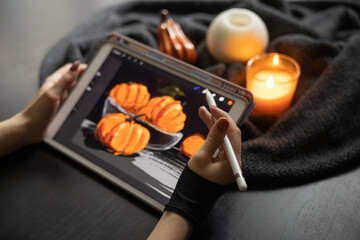 Girl's hand in special glove draws still life picture with pumpkins on electronic tablet near burning candle. The concept of inspiration, creativity, modern art. Halloween, Thanksgiving day