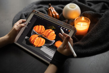 Girl's hand in special glove draws still life picture with pumpkins on electronic tablet near burning candle. The concept of inspiration, creativity, modern art. Halloween, Thanksgiving day