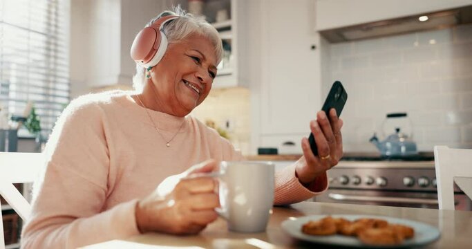 Senior woman, home and headphones with phone, coffee and funny video call, social media or streaming comedy. Elderly person laughing, happy and listening to mobile podcast or meme with tea in kitchen