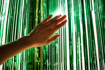 Obraz premium Shimmer shiny green tinsel for Christmas in female hand. A curtain for home decor made of foil. New Year 2024. A girl, woman decorating a room for winter holidays Carnaval, fiesta, festival decoration
