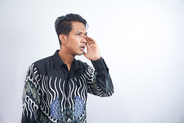 Young asian man wearing batik whispering and gossiping, side view isolated on white