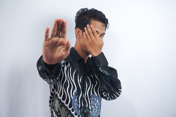 young handsome man covering face with hand and putting other hand up front to stop camera, refusing...