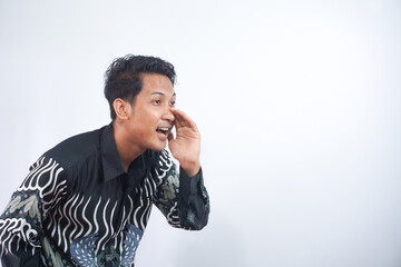 Young asian man wearing batik whispering and gossiping, side view isolated on white