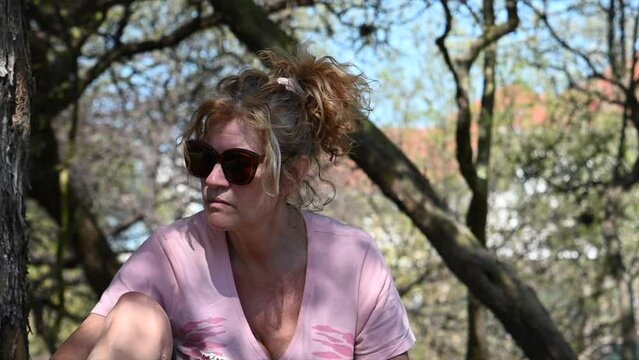 slow motion video of a woman in the shadows of a tree with light hair wearing sunglasses in nature
