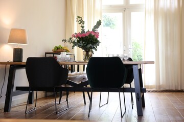 Fototapeta na wymiar Stylish dining room with comfortable furniture, big window and bouquet of roses
