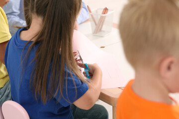 Obraz na płótnie Canvas Little girl and boy cutting color paper with scissors at desk, closeup. Kindergarten activities