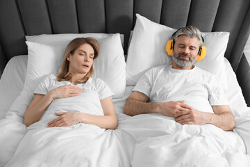 Smiling man with headphones lying near his snoring wife in bed at home