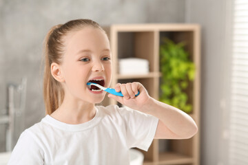 Cute little girl brushing her teeth with plastic toothbrush in bathroom, space for text