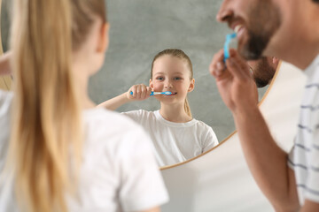 Father and his daughter brushing teeth together near mirror indoors