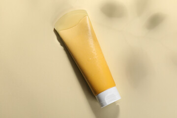 Tube of face cleansing product in water against beige background, top view