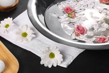Obraz na płótnie Canvas Bowl of water with flowers on dark table, closeup. Pedicure procedure
