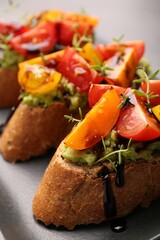 Delicious bruschettas with avocado, tomatoes and balsamic vinegar on gray plate, closeup