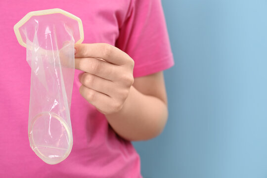 Woman with unrolled female condom on light blue background, closeup. Space for text