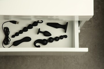 Black vibrator, anal plugs and beads in drawer indoors, top view. Sex toys