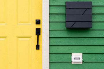 A vibrant yellow colored solid metal door with a black handle and deadbolt lock on a green wooden...