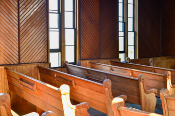 Interior of a vintage church with wooden pews or benches of red wood. The sun is shining in the...