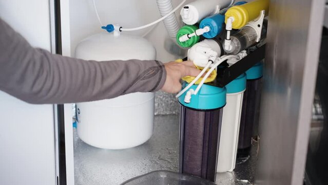 A man is using a cloth to wipe up the water that has leaked from the filter under the kitchen sink.