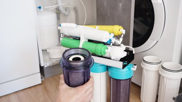 Replacing the pre-filter in a reverse osmosis water purification system. A man has unscrewed the transparent housing with the old filter.