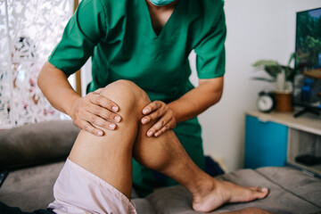 Physiotherapist treating injured knee of male patient, home therapy service