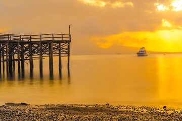 A wooden pier juts out into a calm body of water, bathed in the golden light of sunrise.
