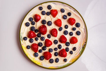 Fresh juicy strawberries and blueberries blueberries in thick whipped cream in a plate on the table