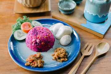 Pink fried rice made from dragon fruit served with tempeh, kerupuk crackers, chicken floss, and vegetables