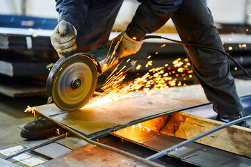 Worker cuts metal with abrasive disk in plant workshop - obrazy, fototapety, plakaty