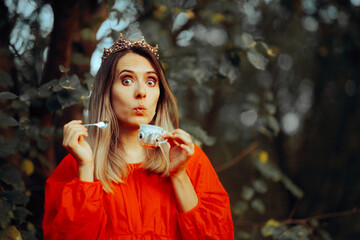Funny Queen Drinking Tea Outdoors in her Garden. Woman wearing a princess costume having a warm tea 
 - obrazy, fototapety, plakaty