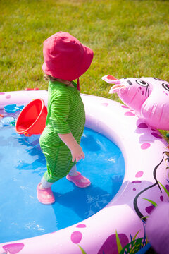 Cute little toddler girl standing in the middle of a kiddie swimming pool in a fun swimsuit and pink hat