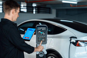Young man travel with EV electric car to shopping center parking lot charging in downtown city...