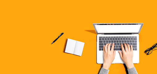 Person using a laptop computer with a notebook and eyeglasses - Flat lay