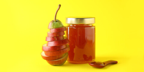 Glass jar of tasty jam and cut pear on yellow background