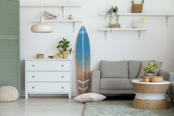 Interior of light living room with surfboard, commode and sofa