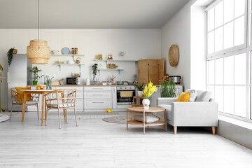 Interior of light kitchen with stylish fridge, counters, shelves, table and sofa