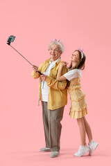 Little girl with her grandmother in crowns taking selfie on pink background