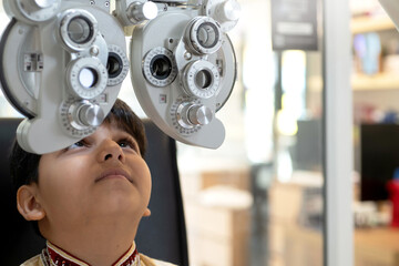 Indian boy in traditional cloth interesting optical phoropter during eye exam, ophthalmological clinic