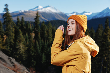 Woman smiling with teeth looking at the mountains in a yellow raincoat with red hair on a hike standing in front of the mountains in a yellow winter sunset cap