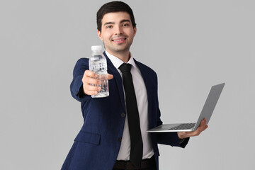 Young businessman with bottle of water and laptop on grey background