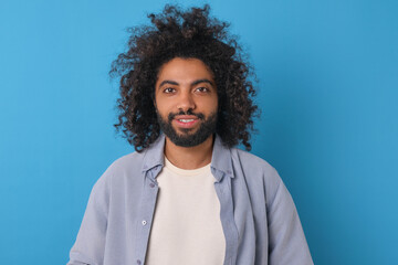 Fototapeta na wymiar Young happy curly Arabian man with smile looking at camera posing for student photo album or advertising poster dressed in casual t-shirt and shirt stands on isolated blue background.