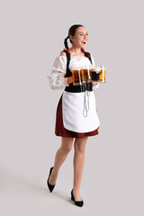 Young woman in traditional German clothes with beer on grey background